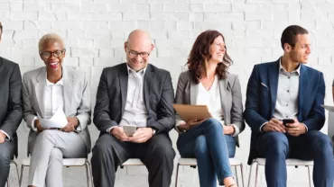 Grupo de pessoas sentadas em fila, vestidas formalmente e sorrindo.