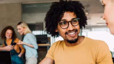 Homem negro de cabelo cacheado sorrindo para a colega de trabalho