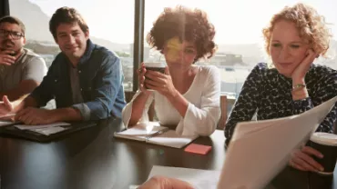 Grupo de pessoas de diversas etnias conversando sobre trabalho sentados em uma mesa