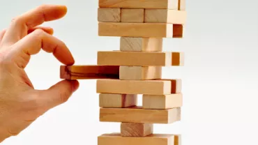 mão humana colocando uma peça em um quebra cabeça em formato de torre, dando a ideia de construção. 