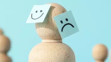 Boneco de madeira com post-its, um feliz e outro triste.