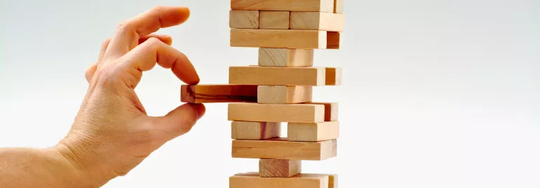 mão humana colocando uma peça em um quebra cabeça em formato de torre, dando a ideia de construção. 